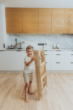 Barn heldur á samanbrjótanlegum Montessori hjálparturn, klappturn í fallegu eldhúsi.