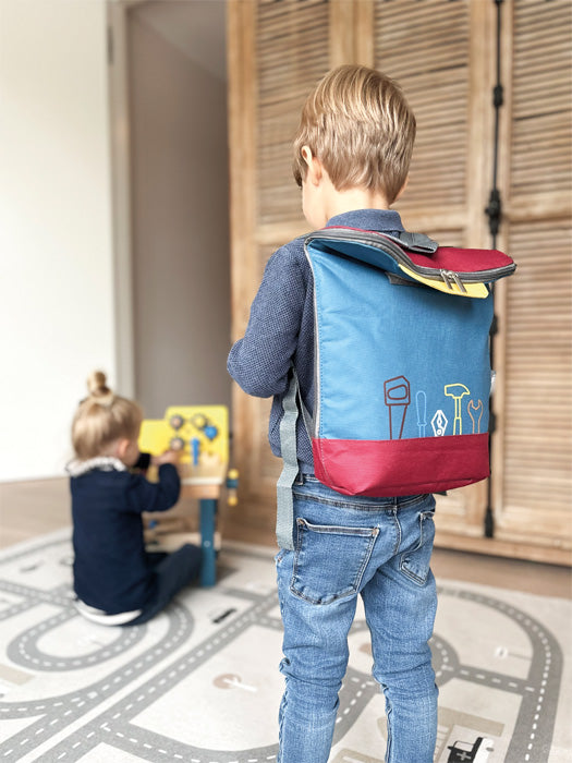 Strákur með verkfærabakpokann á bakinu, annað barn við vinnuborð í bakgrunni