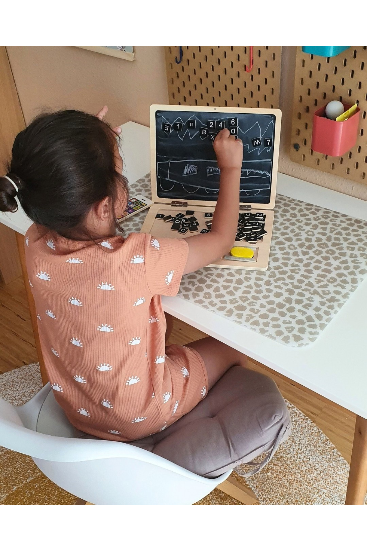 Barn að leika með viðarfartölvu í rúmi með bókum og skrauti í kring