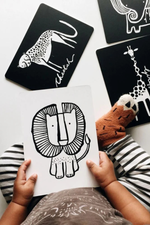 Children's hands holding a card with a lion illustration, surrounded by black cards with animal illustrations on a light background.