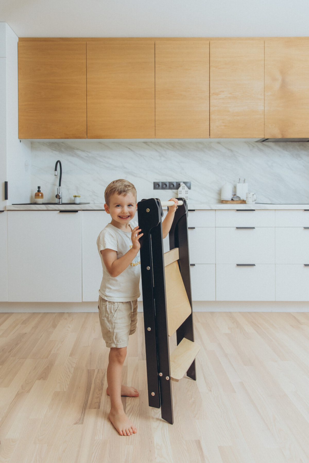 Nærmynd af barni sem heldur um handrið á viðarhjálparturni með svörtum hliðum.