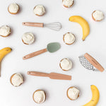 Kiddikutter eldunarsett með muffins og banönum á hvítum bakgrunni – leikandi eldamennska fyrir börn.