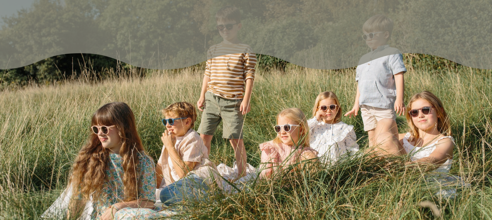 Börn með Leosun sólgleraugu sitja og standa í grasi utandyra í sumarstemningu 