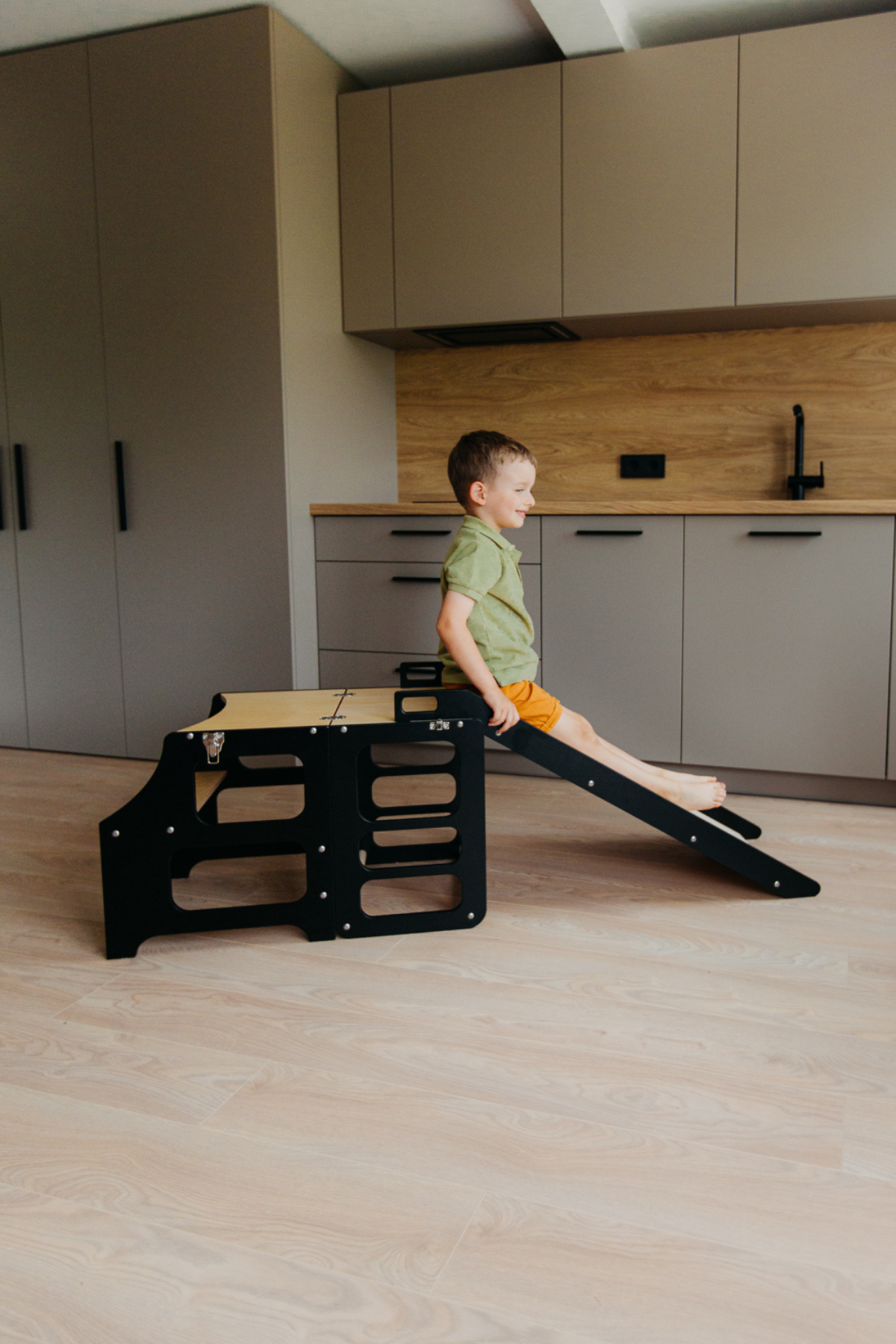 Barn að leika sér á svörtum Step and Slide hjálparturni með rennibraut í eldhúsi