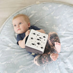 Baby lying on a mat holding a book with black fish illustrations