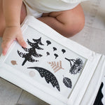 Child holding a white board with black leaf designs on a light wooden floor.