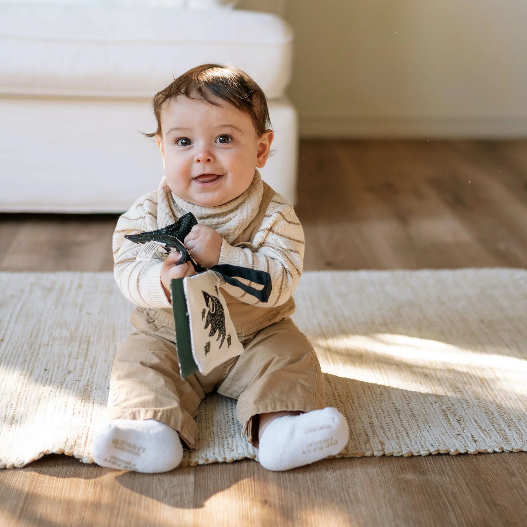 Baby sitting on a rug holding a book with a bow tie