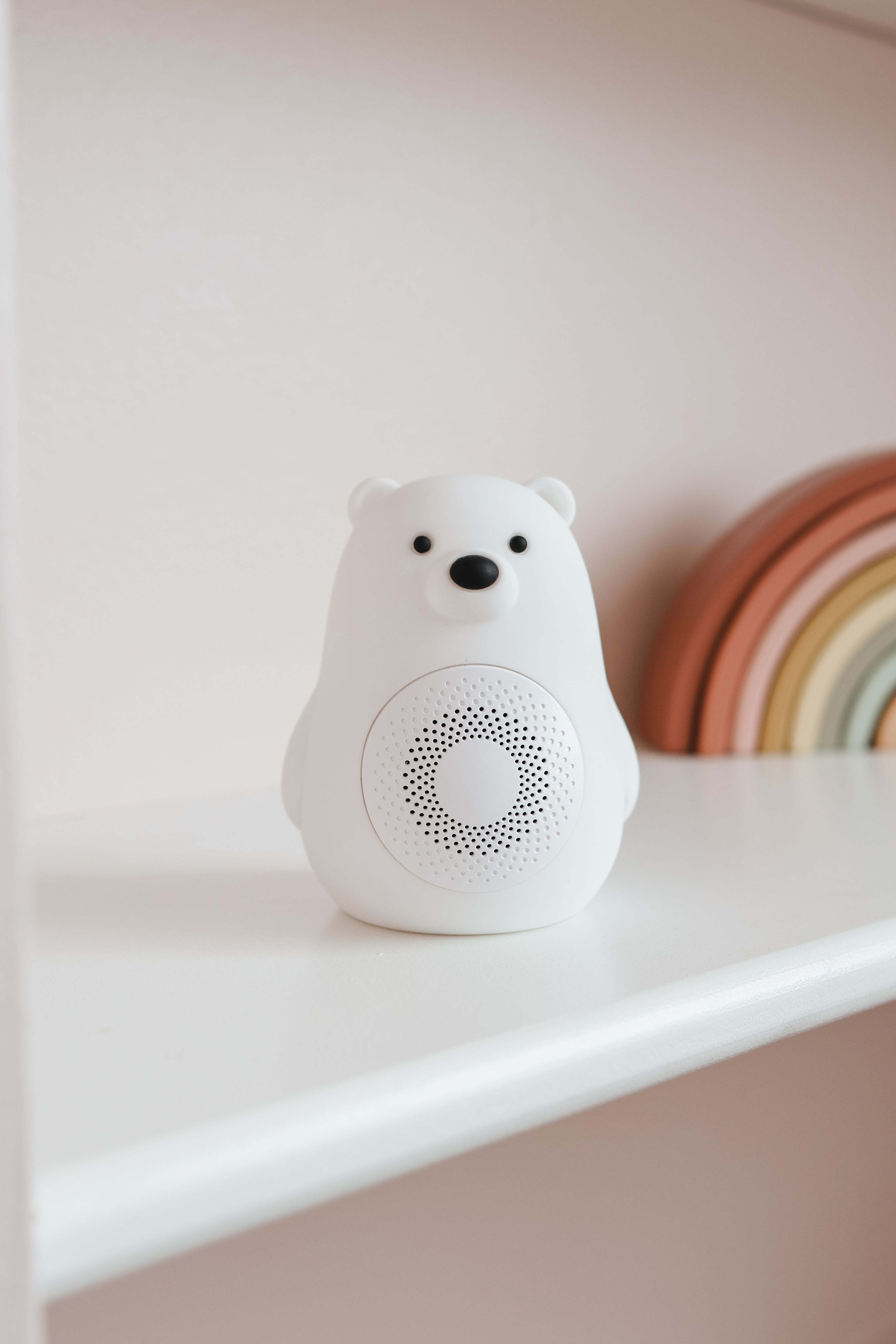 White noise tæki í bjarnarformi á hvítu borði með bleikum vegg að baki.