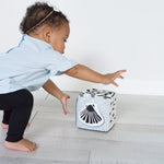 Child reaching towards a toy box with a shell design on a light wooden floor.