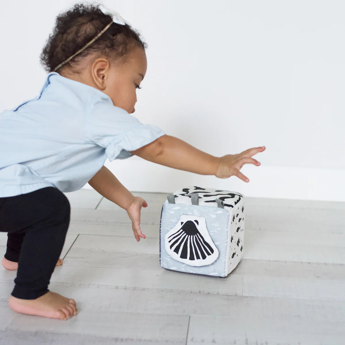Child reaching towards a toy box with a shell design on a light wooden floor.