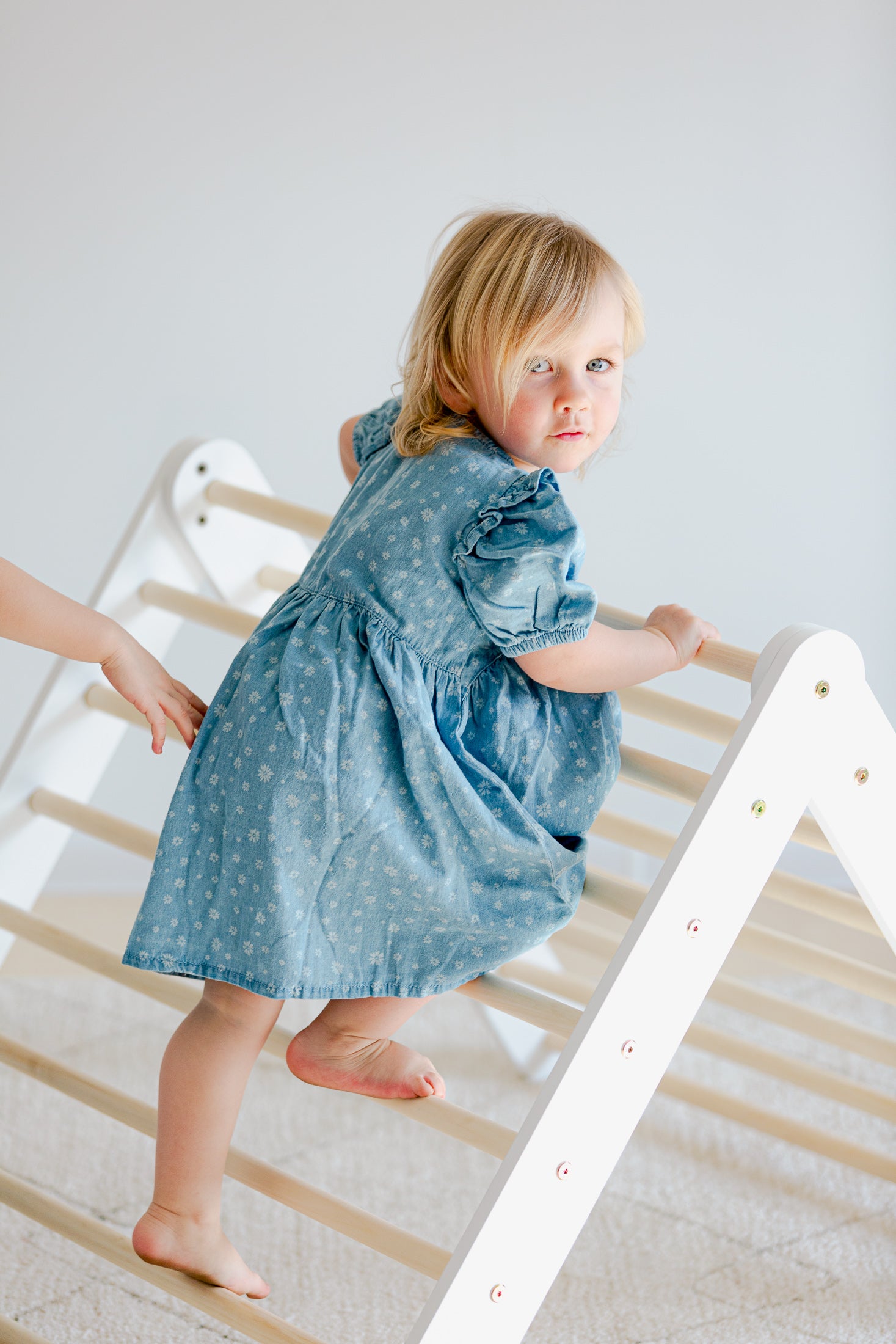 Barn að leika við hvítan klifurþríhyrning með rennibraut – örugg hreyfing og gleði.