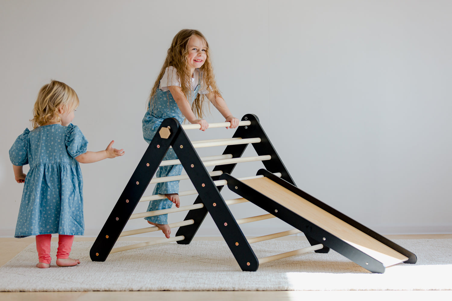 Tvær stelpur leika sér við svartan pikler klifurþríhyrning frá Duck WoodWorks