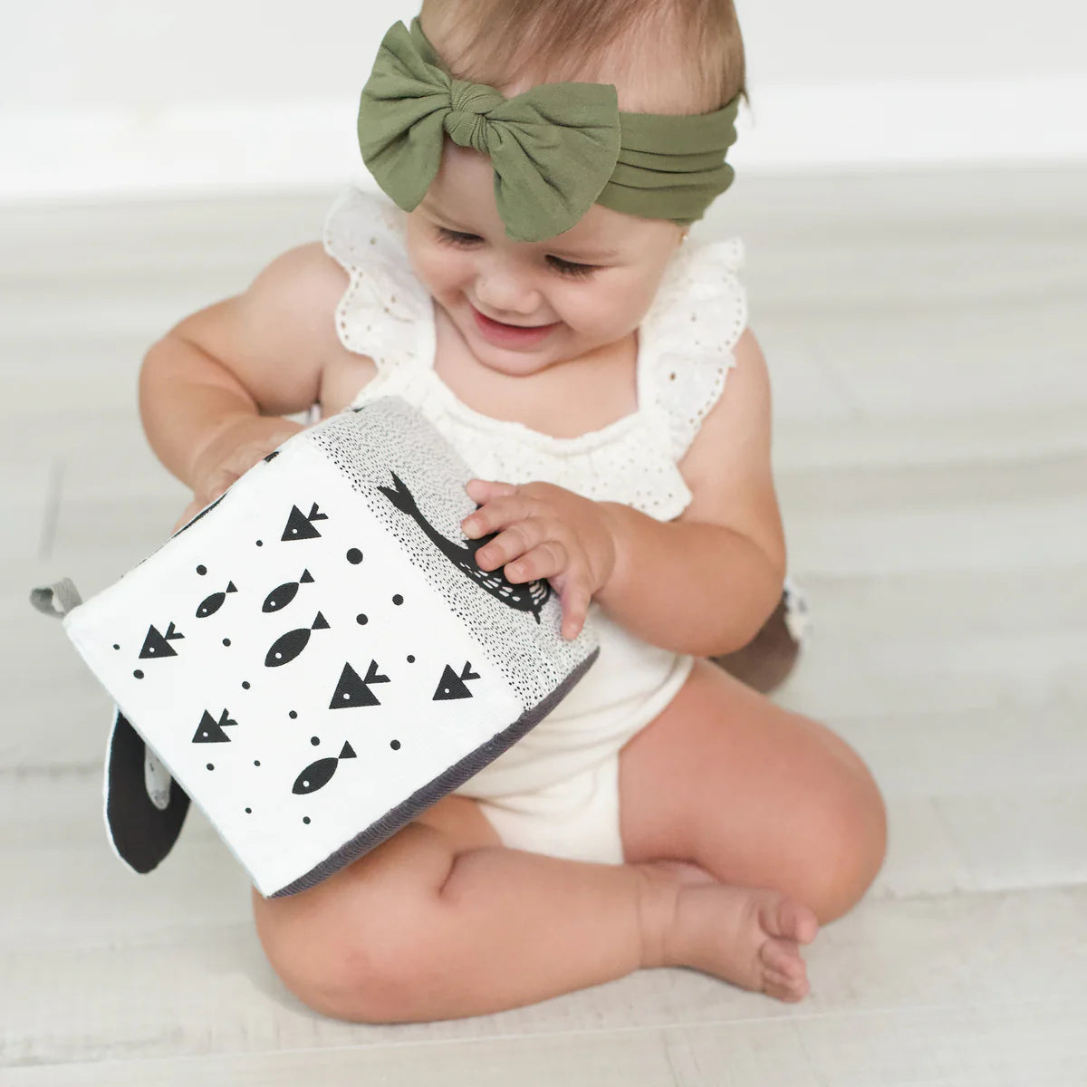 Baby holding a black and white book with a green headband