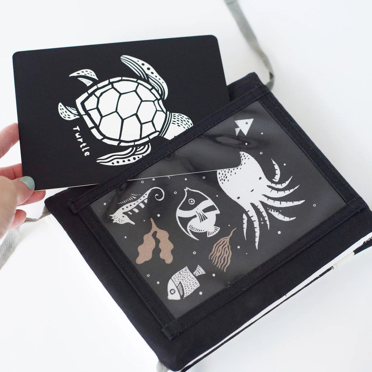 Tummy Time Gallery with white sea creature illustrations held by a hand on a light background